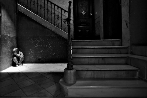 Sad and lonely kid crouching in a corner